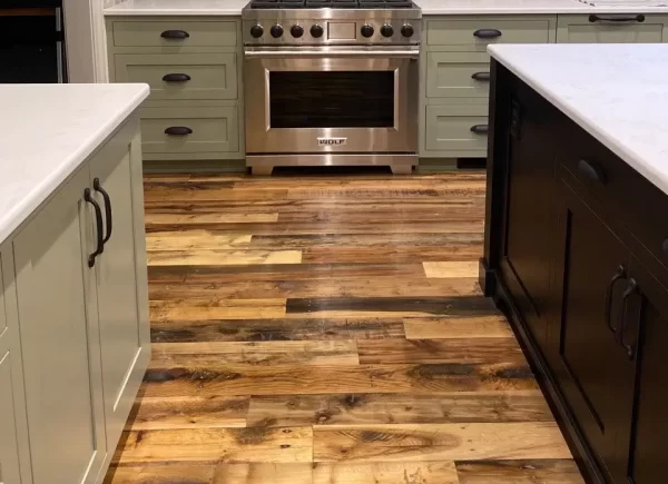 Industrial oak engineered flooring with deep character marks featured in a modern kitchen with sage green cabinetry and marble countertops.