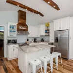A bright farmhouse kitchen with reclaimed oak engineered flooring, rustic ceiling beams, and a modern center island with bar stools.