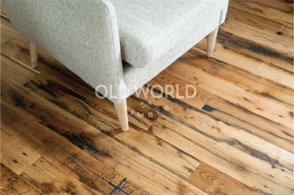 Reclaimed engineered oak flooring with blackened saw marks beneath a beige armchair, reflecting its industrial past.