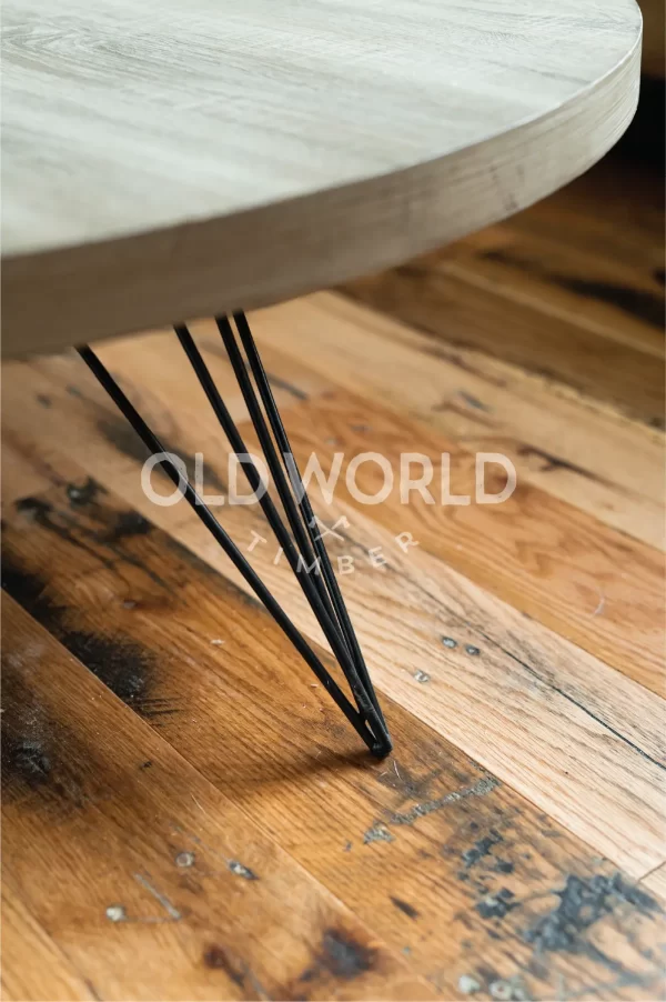 Detailed view of reclaimed Industrial Oak flooring with heavy character marks, under a round wood-and-metal coffee table.