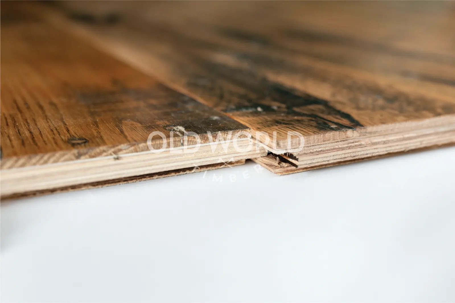 Close-up of the layered structure of engineered reclaimed oak flooring showing the solid oak wear layer and plywood backing.