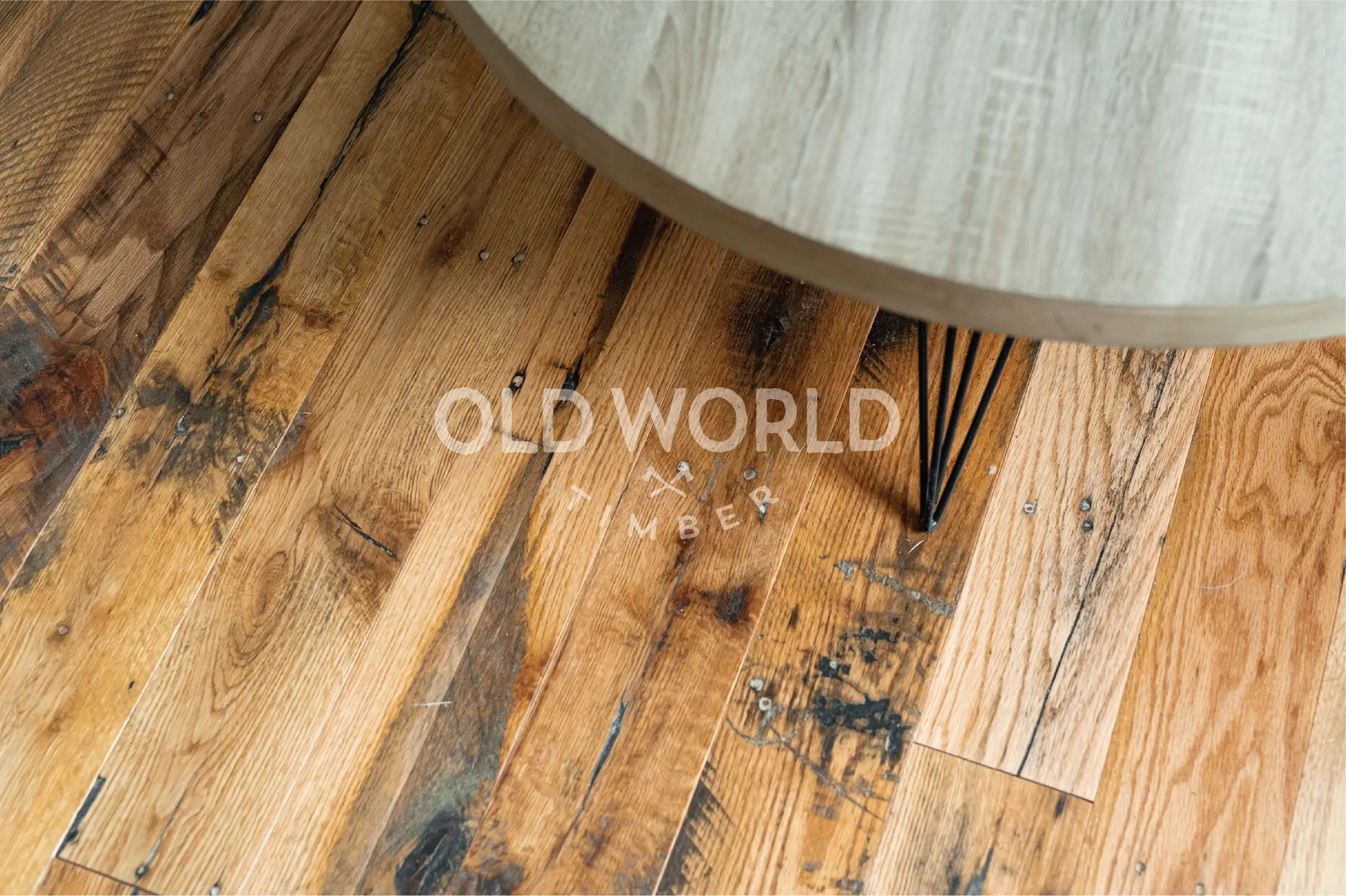 Detailed view of reclaimed Industrial Oak flooring with heavy character marks, under a round wood-and-metal coffee table.