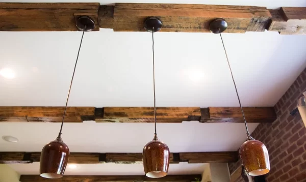 a white ceiling with brown wood beams with three hanging brown lamps