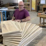 A woodworker in a wood workshop holding uninstalled reclaimed wood stair treads
