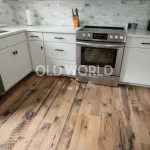 Bright modern kitchen with Heartland Barnwood Mixed Oak reclaimed engineered flooring, a round white table, rattan chair, and stainless steel oven and fridge.