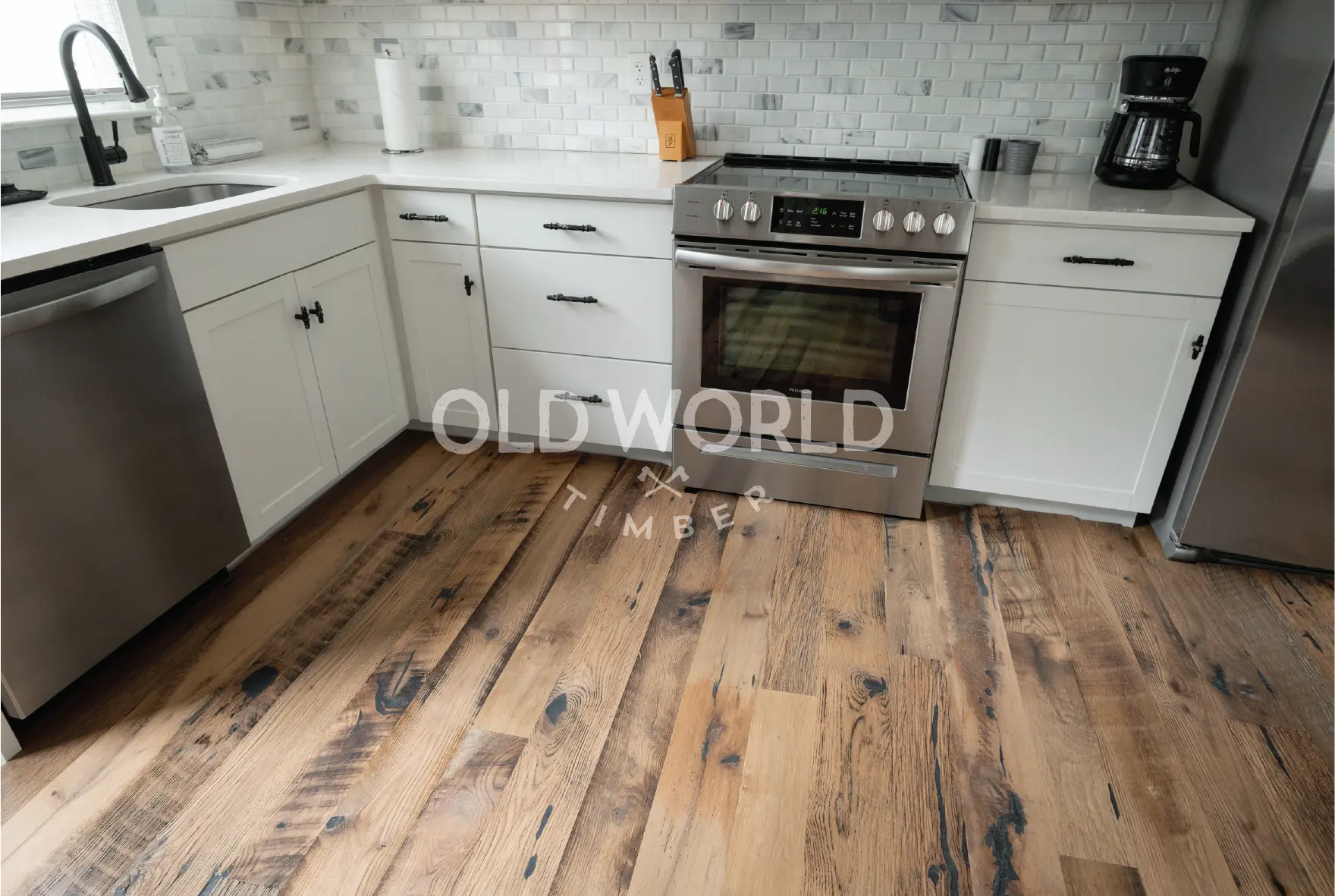 Bright modern kitchen with Heartland Barnwood Mixed Oak reclaimed engineered flooring, a round white table, rattan chair, and stainless steel oven and fridge.