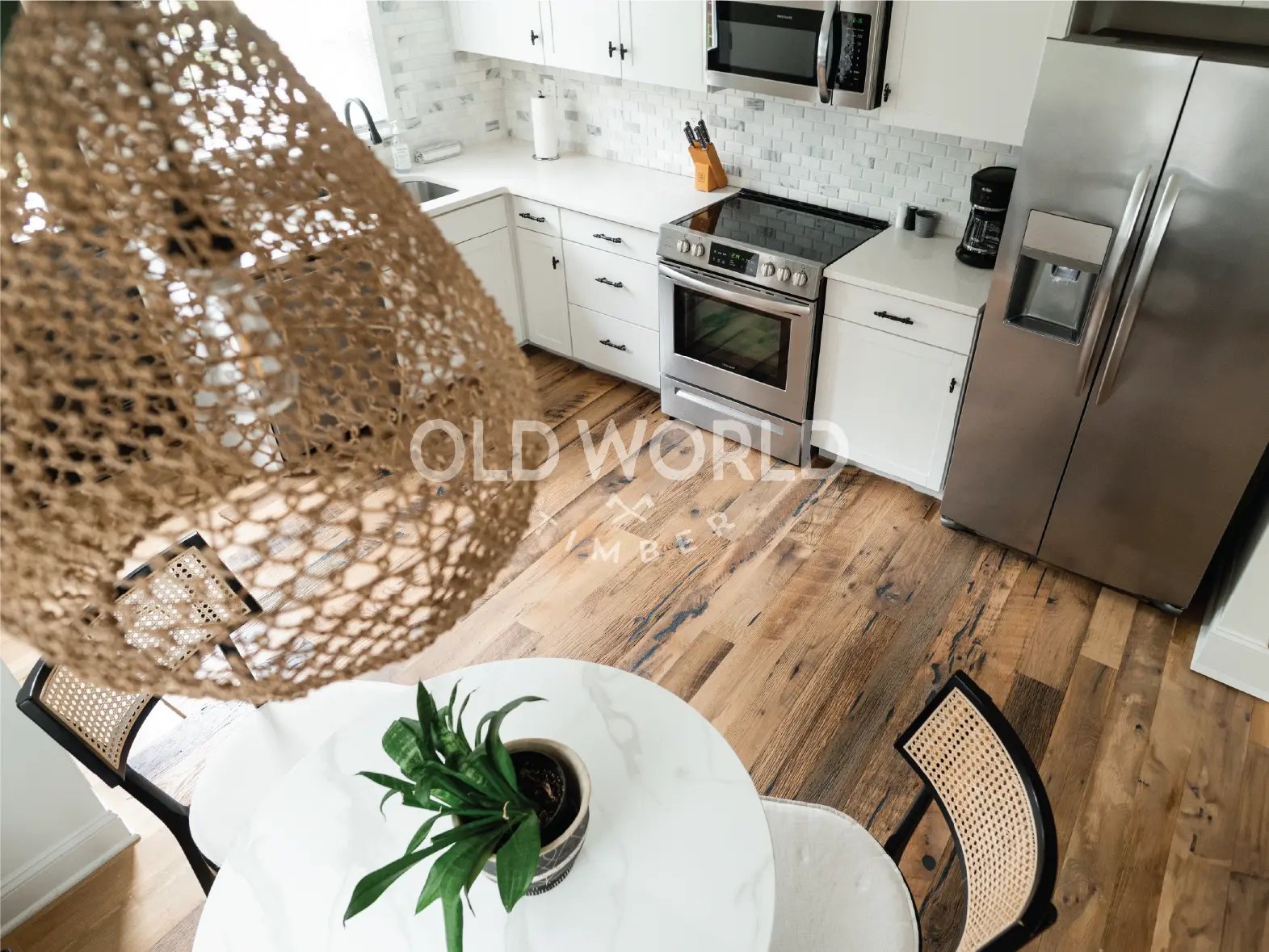 Overhead view of Heartland Barnwood Mixed Oak engineered reclaimed flooring in a white kitchen with marble dining table and woven light fixture.