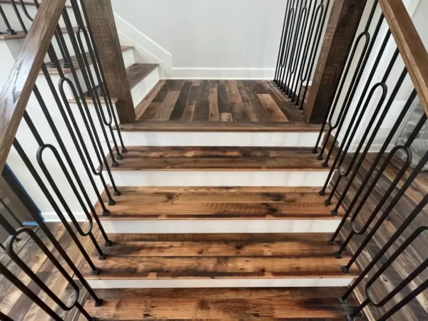 Staircase clad with Heartland Barnwood Mixed Oak engineered reclaimed wood flooring, showcasing rustic tones and black iron railings.