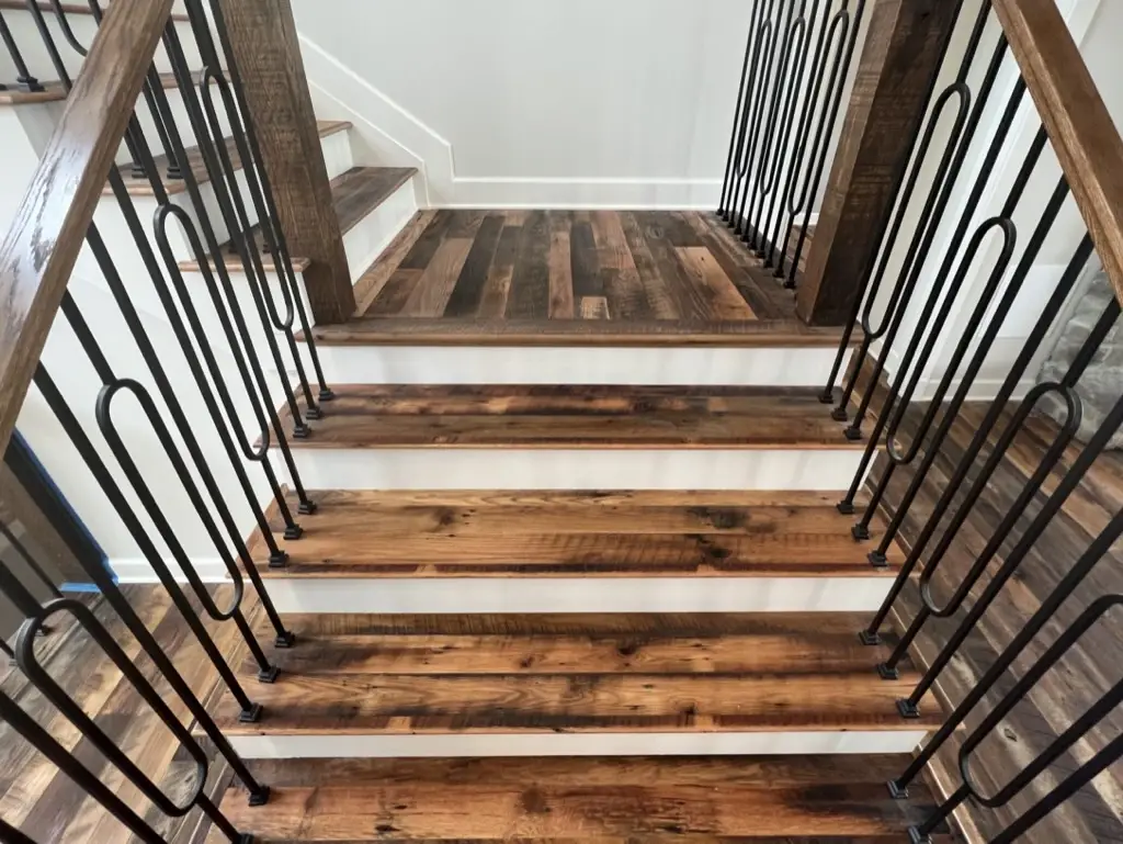 Staircase clad with Heartland Barnwood Mixed Oak engineered reclaimed wood flooring, showcasing rustic tones and black iron railings.