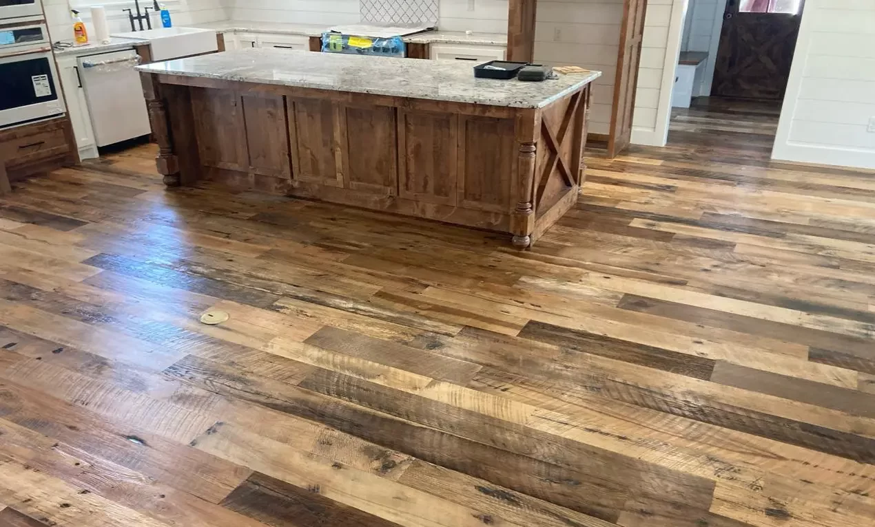 Wide view of Heartland Barnwood Mixed Oak engineered reclaimed flooring in a rustic kitchen with large wood island and granite countertop.