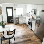Entry view into a white kitchen featuring Old World Timber’s Heartland Barnwood Mixed Oak engineered reclaimed wood flooring.