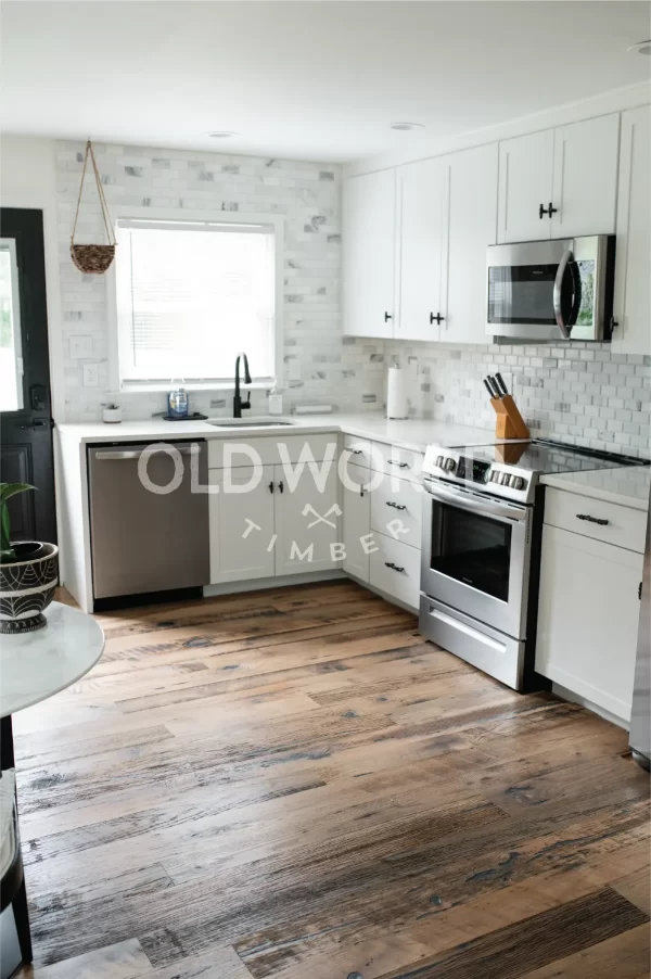 Corner kitchen view showing white cabinetry, stainless appliances, and reclaimed mixed oak flooring with historic texture.