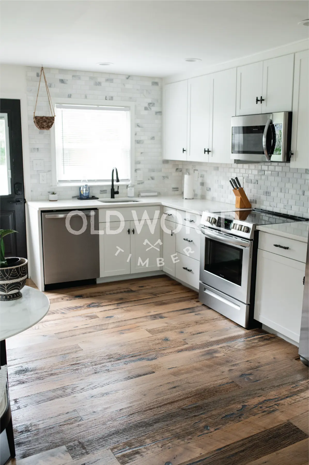 Corner kitchen view showing white cabinetry, stainless appliances, and reclaimed mixed oak flooring with historic texture.