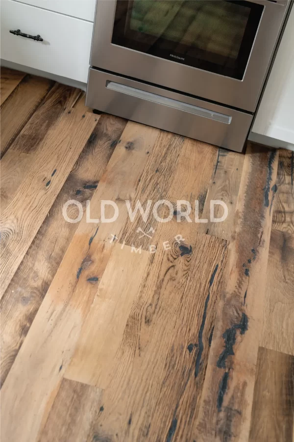 Close-up of reclaimed engineered mixed oak planks with blackened saw marks, patina, and wide grain character near kitchen stove.