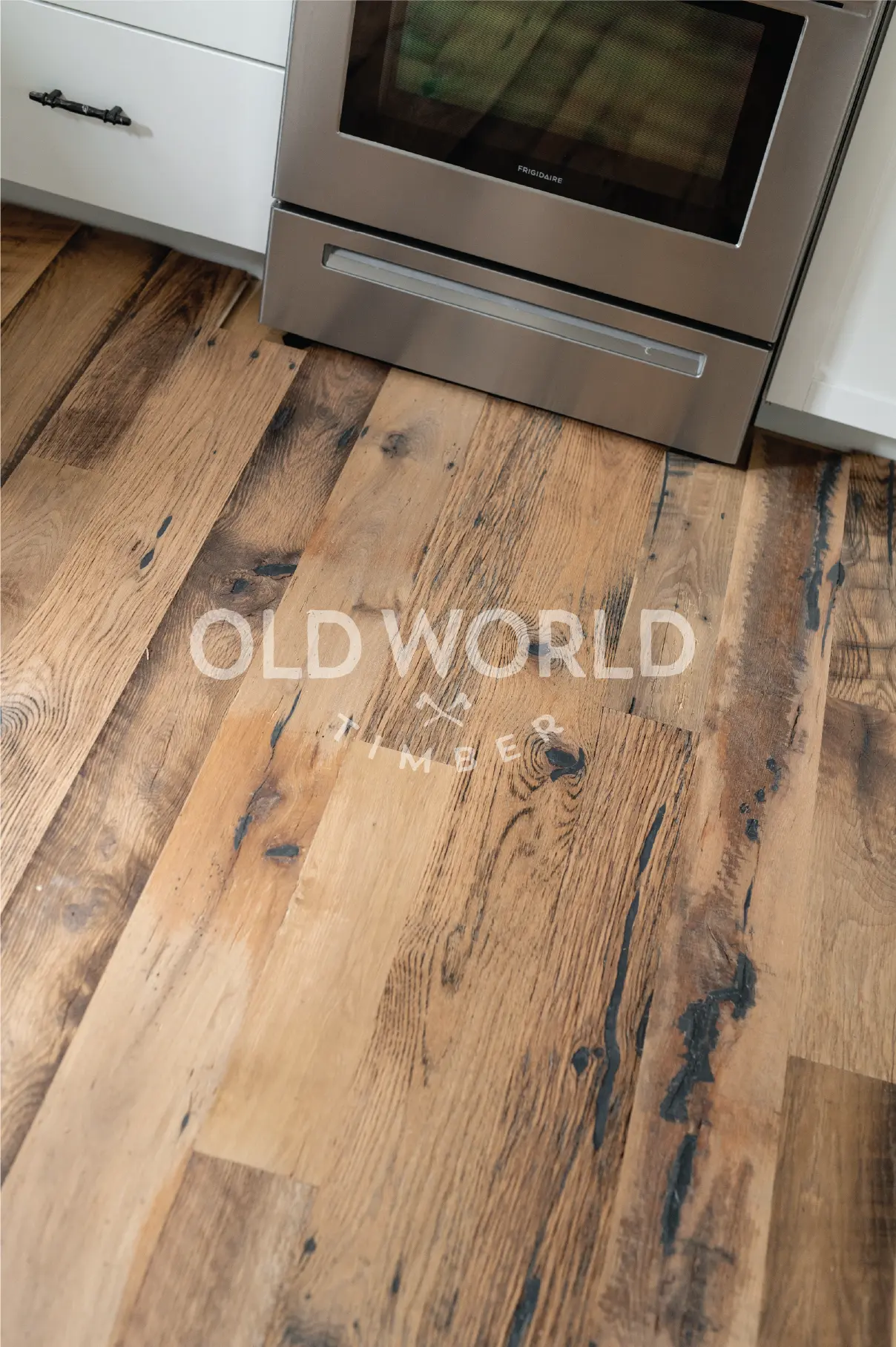 Close-up of reclaimed engineered mixed oak planks with blackened saw marks, patina, and wide grain character near kitchen stove.