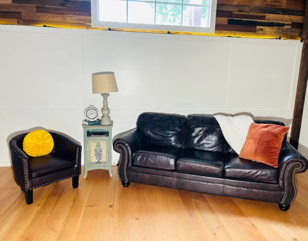 Bright living room featuring reclaimed Douglas Fir clean vertical grain engineered flooring, paired with dark leather sofa and accent chair under natural light.