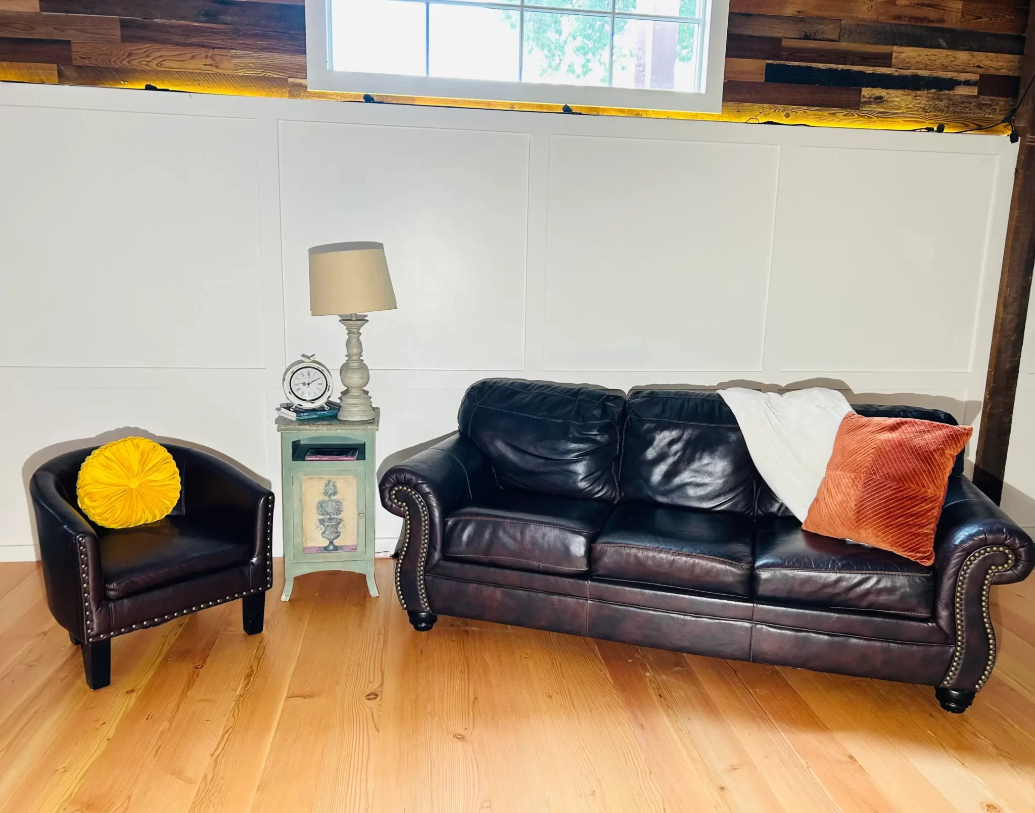 Bright living room featuring reclaimed Douglas Fir clean vertical grain engineered flooring, paired with dark leather sofa and accent chair under natural light.