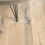 Industrial Oak Clean Face White Oak engineered planks beneath a round wood-and-metal coffee table, showing subtle distressing and organic mineral streaks.