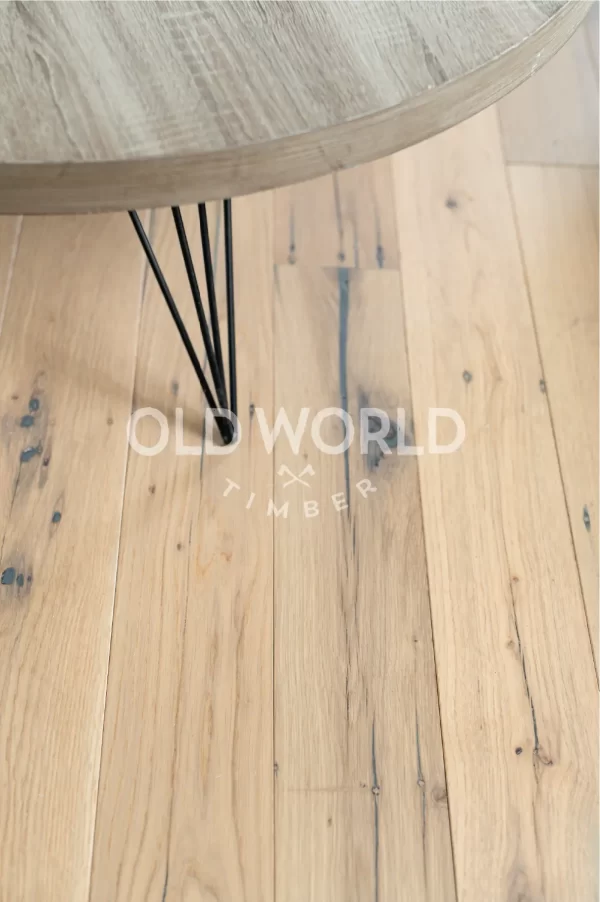 Industrial Oak Clean Face White Oak engineered planks beneath a round wood-and-metal coffee table, showing subtle distressing and organic mineral streaks.
