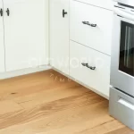 Close-up view of reclaimed white oak flooring paired with white cabinetry and black hardware in a modern kitchen corner.