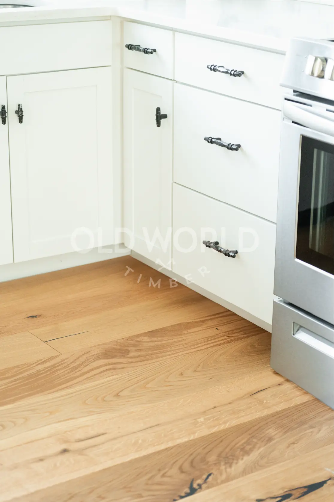 Close-up view of reclaimed white oak flooring paired with white cabinetry and black hardware in a modern kitchen corner.