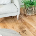 Grey armchair and potted greenery over warm oak tones of Modern Harvest engineered flooring, showcasing knots and sustainability appeal.