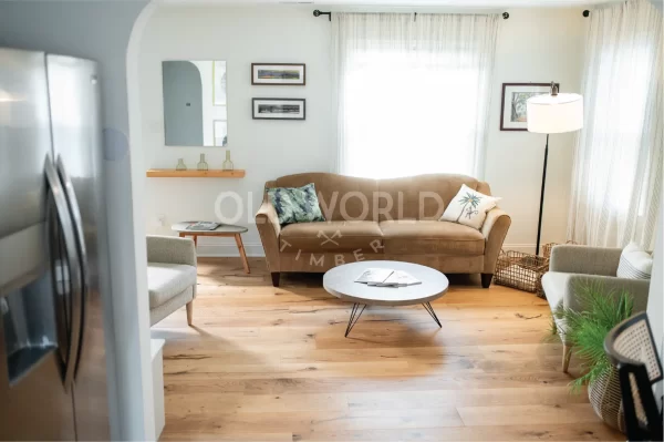 Wide living room shot with a warm brown couch and Modern Harvest engineered flooring, featuring eco-friendly oak planks with soft character marks.
