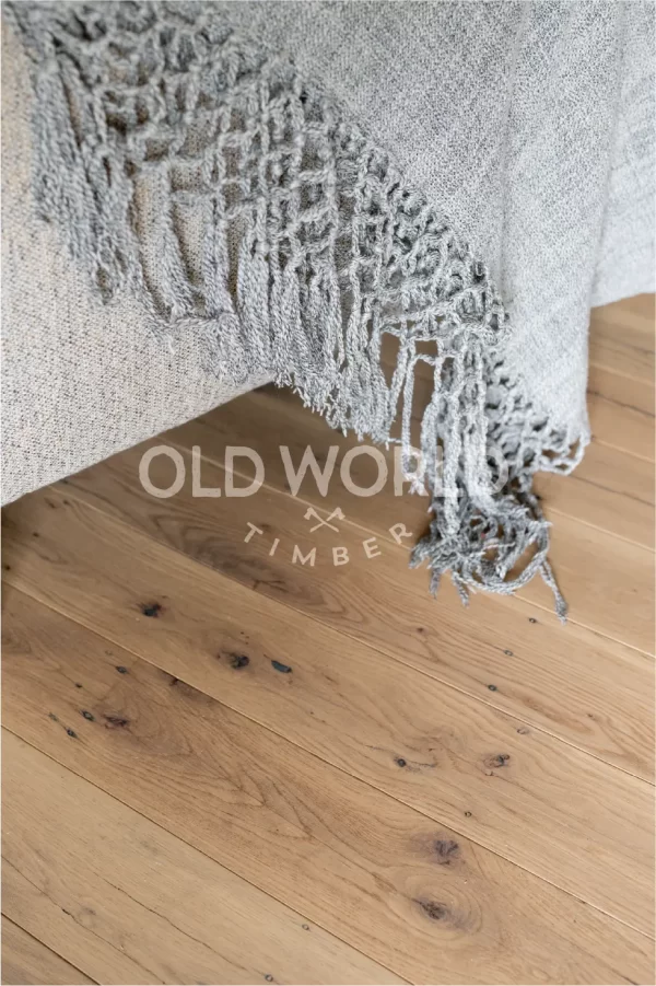 Detailed image of reclaimed white oak flooring beneath a textured gray throw, showing the natural beauty and imperfections of antique hardwood.