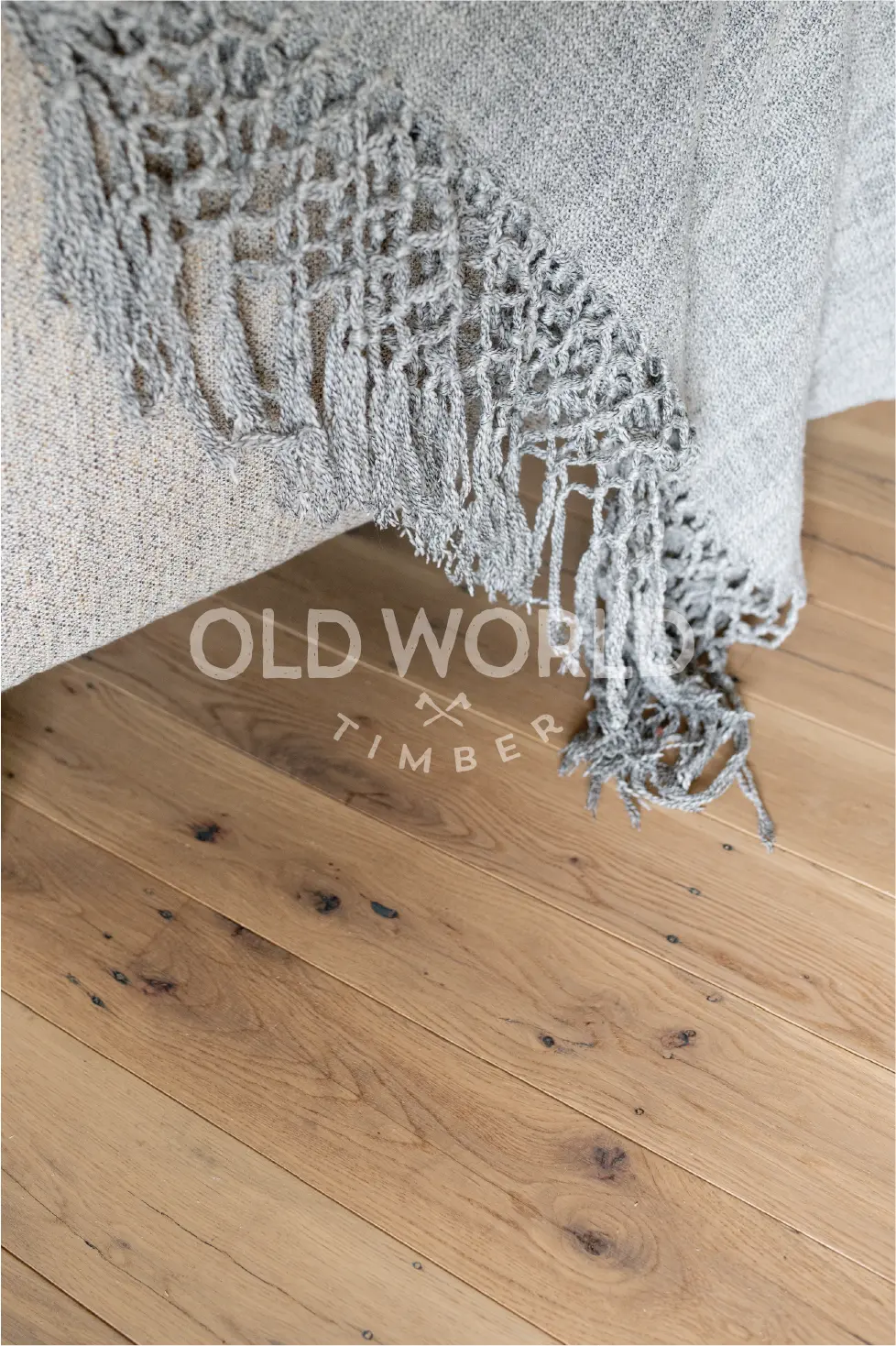 Detailed image of reclaimed white oak flooring beneath a textured gray throw, showing the natural beauty and imperfections of antique hardwood.