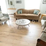 Close-up of reclaimed industrial oak engineered floors with visible saw marks and dark knots beneath a brown couch and modern end table.