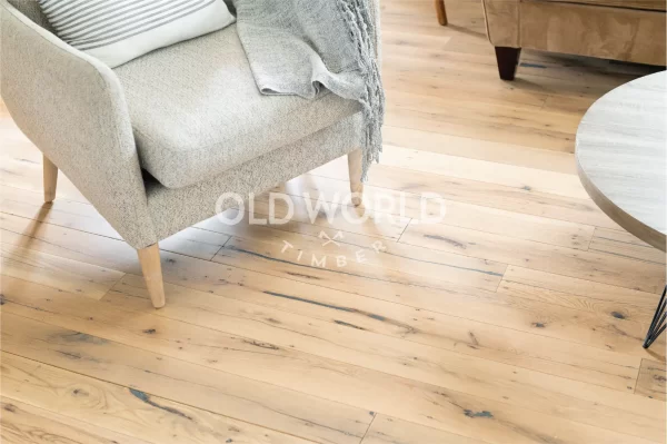 Wide shot of light-toned white oak engineered flooring with reclaimed characteristics, featuring subtle cracks and grain under a modern chair and coffee table.