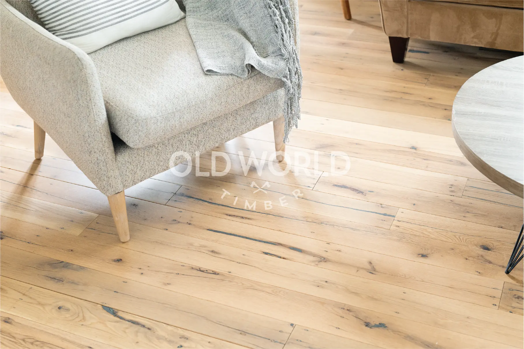 Wide shot of light-toned white oak engineered flooring with reclaimed characteristics, featuring subtle cracks and grain under a modern chair and coffee table.