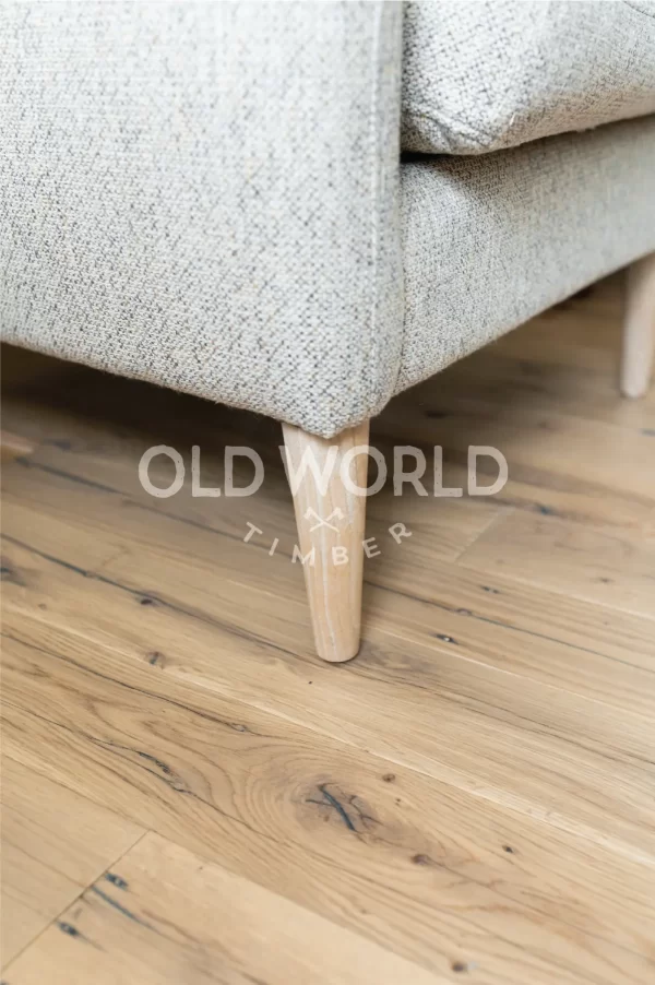 Close-up of Industrial Oak Clean Face flooring made from reclaimed hardwood, highlighting organic knots and dark grain streaks under a neutral textured chair.