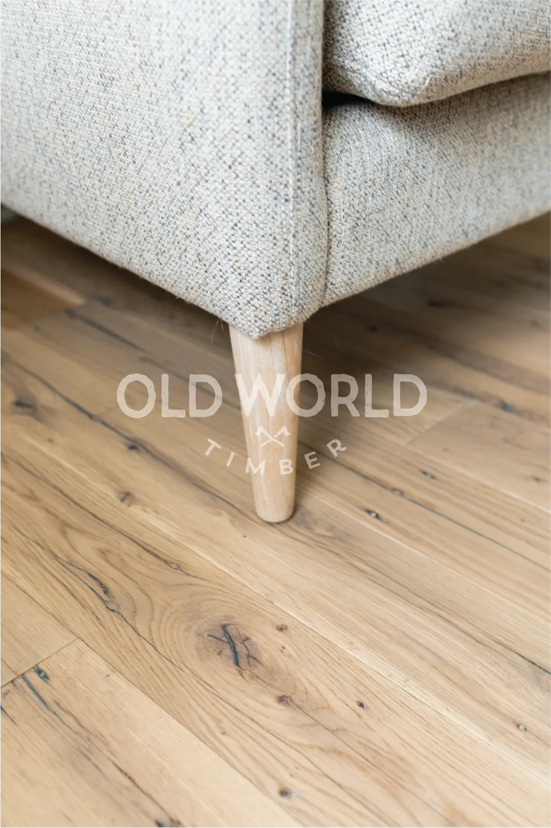 Detailed view of reclaimed white oak engineered flooring featuring natural grain patterns and light distress marks beneath a light gray upholstered armchair.