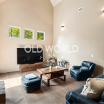 Wide-plank rift and quartered oak flooring in a hallway leading to a bright living room with exposed beams.