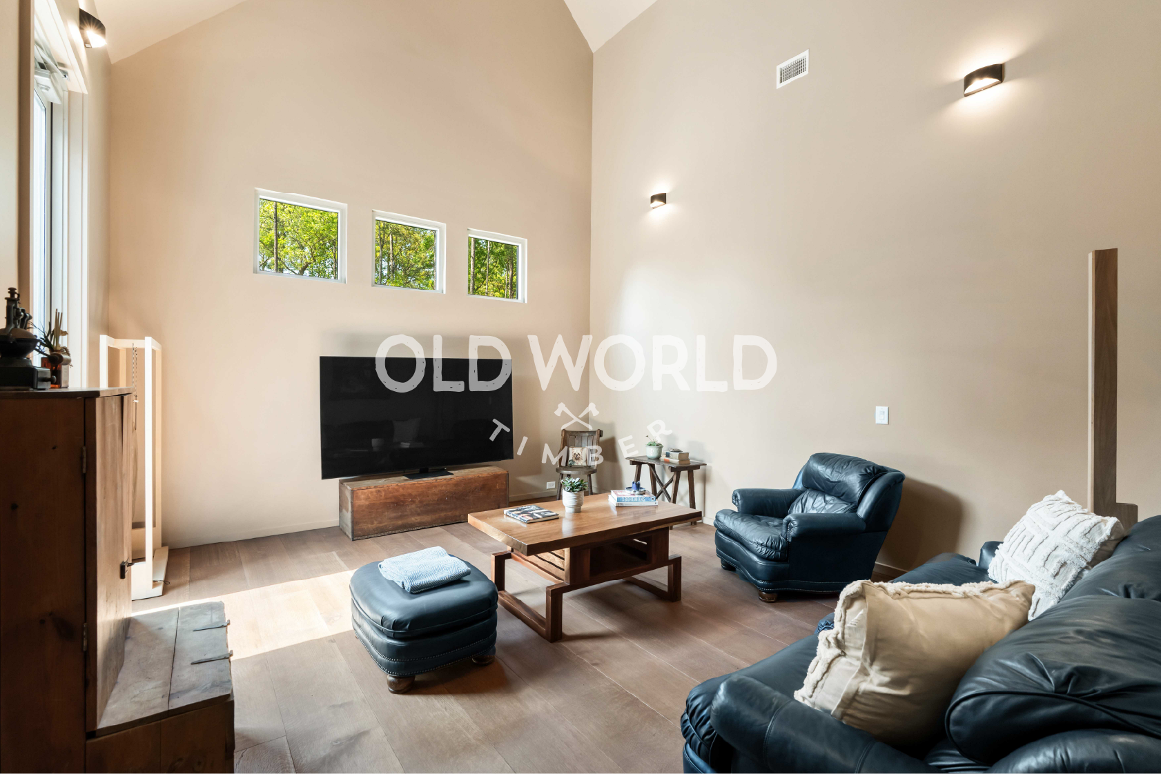 Wide-plank rift and quartered oak flooring in a hallway leading to a bright living room with exposed beams.